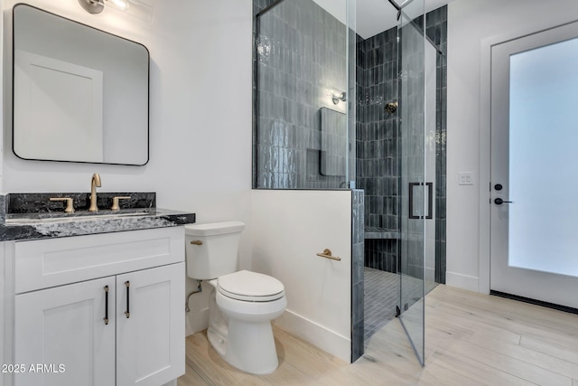 bathroom featuring toilet, wood finished floors, vanity, baseboards, and a shower stall