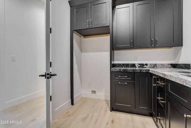 kitchen featuring light stone counters, baseboards, dark cabinetry, and light wood finished floors