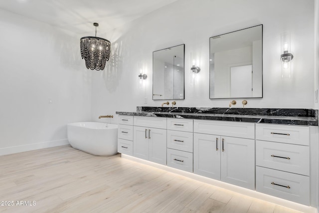 bathroom featuring baseboards, wood finished floors, vanity, a freestanding tub, and a chandelier