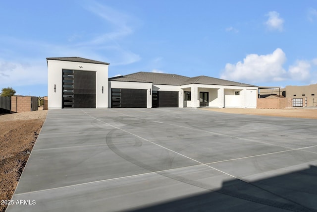 view of front of home featuring a garage, driveway, fence, and stucco siding