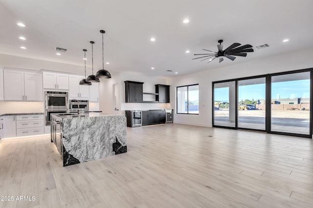 kitchen with double oven, visible vents, white cabinets, a center island with sink, and pendant lighting