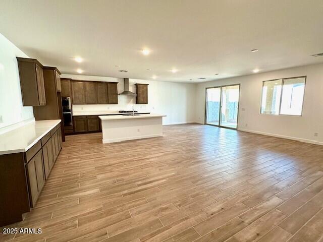 kitchen featuring sink, a kitchen island with sink, wall chimney range hood, and light hardwood / wood-style flooring