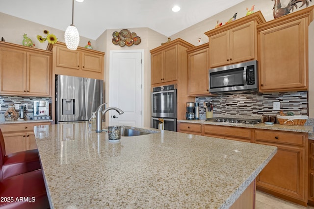 kitchen featuring a center island with sink, decorative backsplash, light stone counters, appliances with stainless steel finishes, and a sink