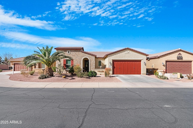 mediterranean / spanish house featuring concrete driveway, stone siding, a tiled roof, an attached garage, and stucco siding