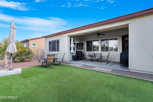 rear view of house with a ceiling fan, a yard, stucco siding, outdoor dining space, and a patio area