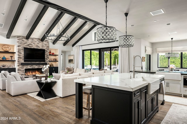 kitchen with hanging light fixtures, light stone countertops, plenty of natural light, and a kitchen island with sink