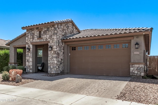 view of front of home with stone siding, a tiled roof, decorative driveway, and an attached garage