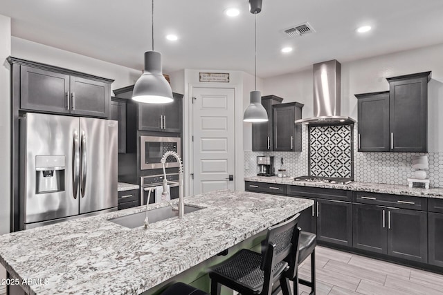 kitchen featuring stainless steel appliances, wall chimney exhaust hood, a sink, a breakfast bar, and tasteful backsplash