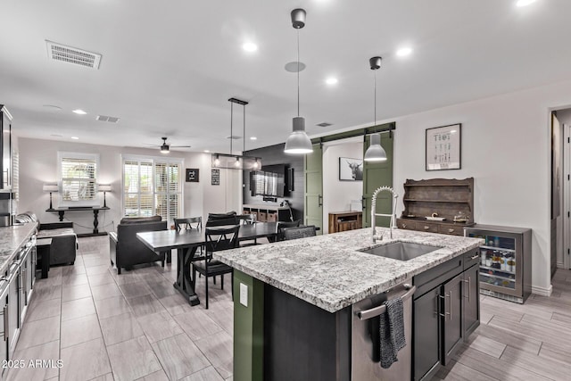 kitchen featuring a sink, beverage cooler, open floor plan, ceiling fan, and a center island with sink