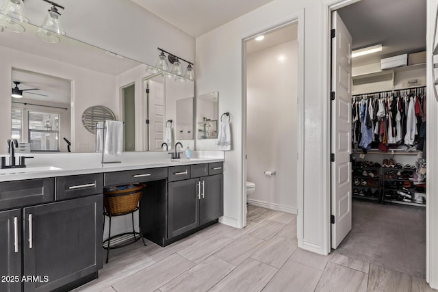 bathroom with toilet, a ceiling fan, double vanity, and a walk in closet