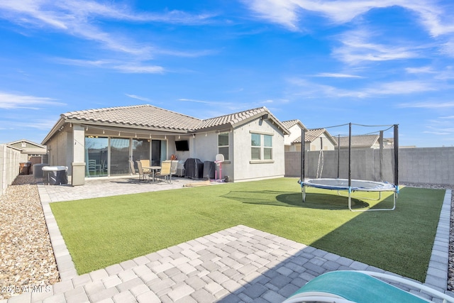 rear view of house featuring a trampoline, a patio area, and a lawn