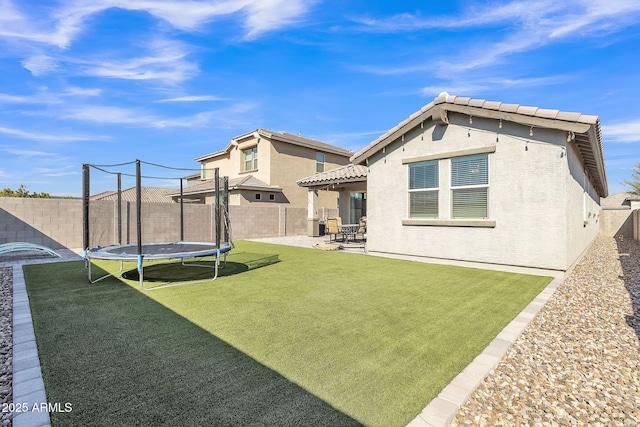 rear view of property with a trampoline, a yard, and a patio area