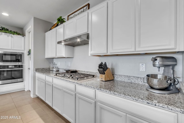 kitchen with appliances with stainless steel finishes, light stone countertops, light tile patterned floors, and white cabinets