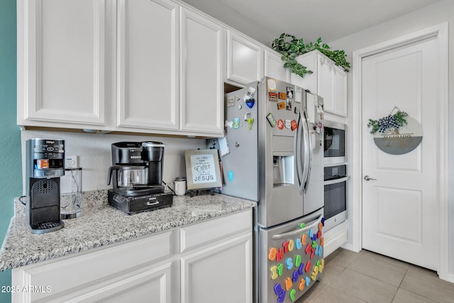 kitchen with white cabinetry, appliances with stainless steel finishes, light tile patterned flooring, and light stone countertops