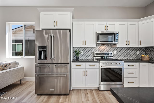 kitchen with appliances with stainless steel finishes, white cabinetry, backsplash, and light hardwood / wood-style flooring