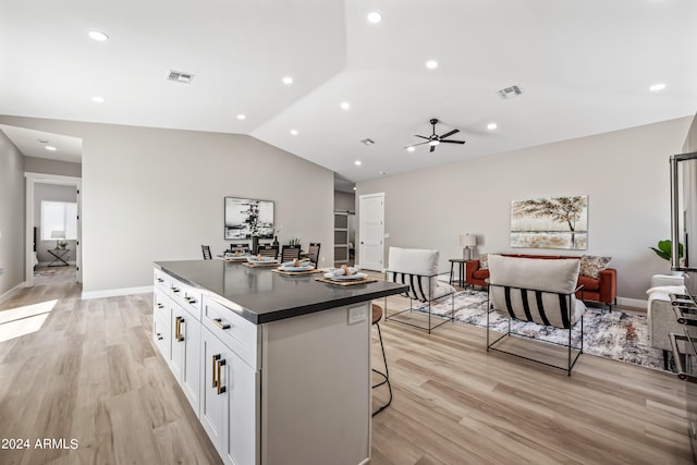 kitchen featuring a center island, white cabinetry, light hardwood / wood-style flooring, ceiling fan, and a kitchen bar