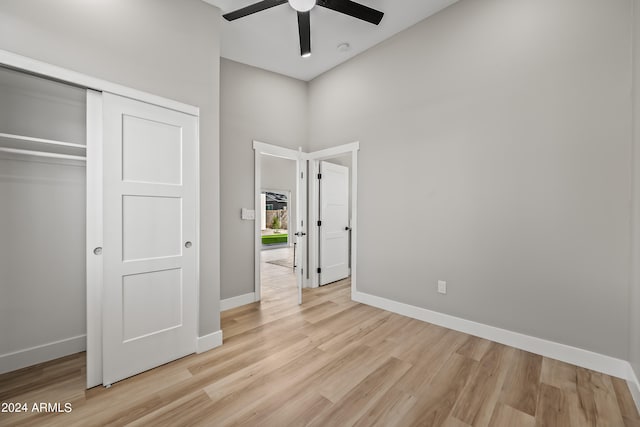 unfurnished bedroom with ceiling fan, a high ceiling, light hardwood / wood-style floors, and a closet