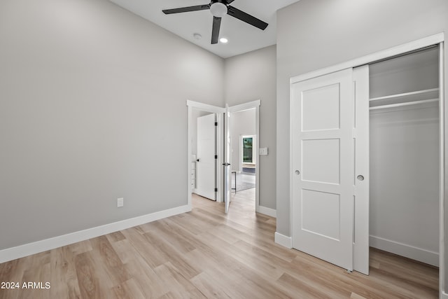 unfurnished bedroom with a high ceiling, a closet, ceiling fan, and light hardwood / wood-style flooring