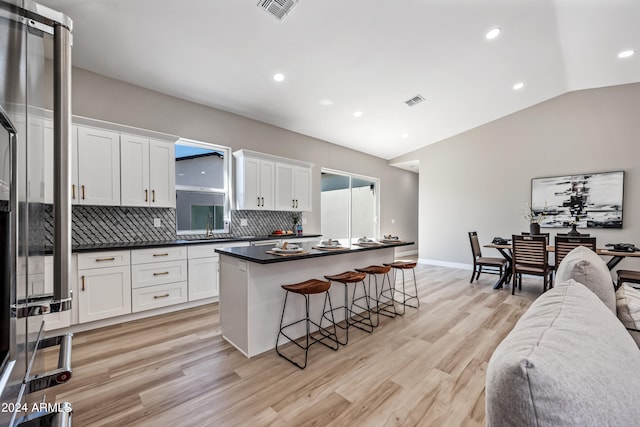 kitchen featuring light hardwood / wood-style floors, white cabinetry, a kitchen island, tasteful backsplash, and vaulted ceiling