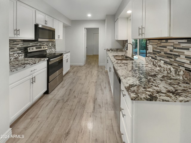 kitchen with light stone counters, white cabinets, sink, stainless steel appliances, and light wood-type flooring