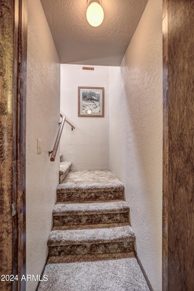 stairway with carpet and a textured ceiling