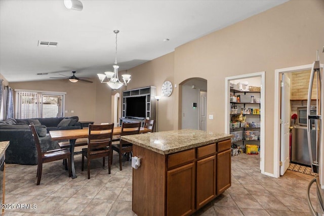 kitchen featuring a center island, light stone countertops, hanging light fixtures, vaulted ceiling, and ceiling fan with notable chandelier