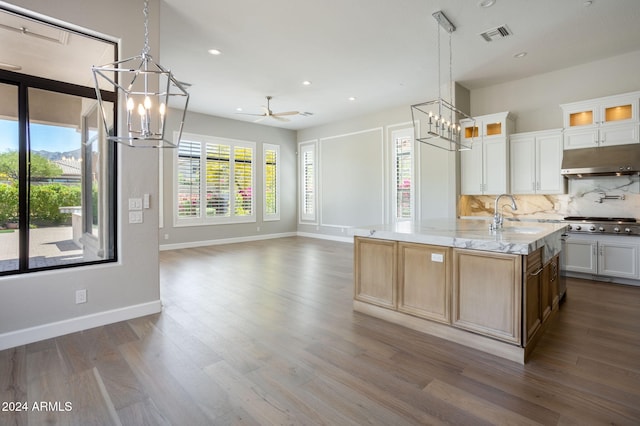 kitchen with light stone counters, ceiling fan with notable chandelier, sink, hardwood / wood-style floors, and white cabinetry