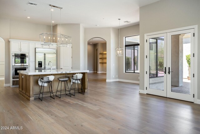 kitchen with a large island, french doors, hanging light fixtures, stainless steel appliances, and white cabinets