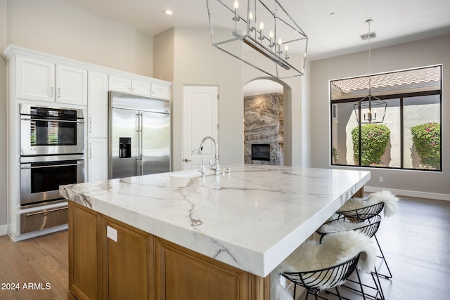 kitchen with white cabinets, a center island with sink, hanging light fixtures, light hardwood / wood-style floors, and stainless steel appliances