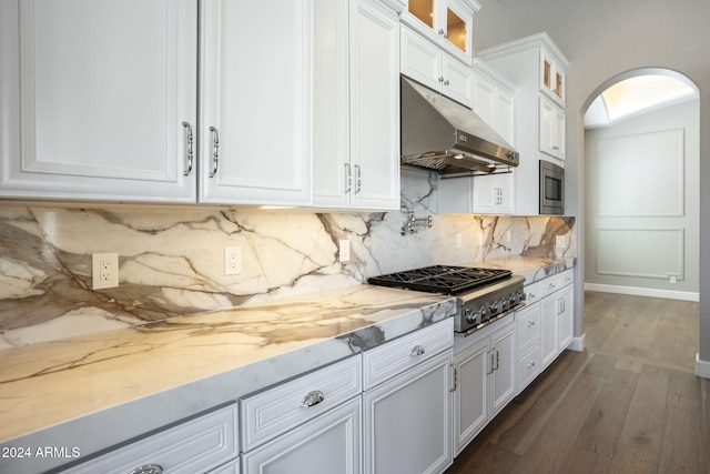 kitchen with appliances with stainless steel finishes, dark hardwood / wood-style flooring, tasteful backsplash, light stone counters, and white cabinetry