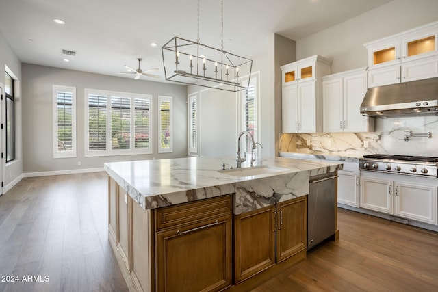 kitchen featuring light stone countertops, stainless steel appliances, hardwood / wood-style floors, white cabinetry, and an island with sink