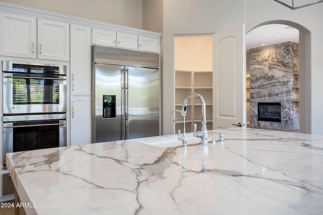 kitchen with a high end fireplace, sink, white cabinets, and stainless steel appliances