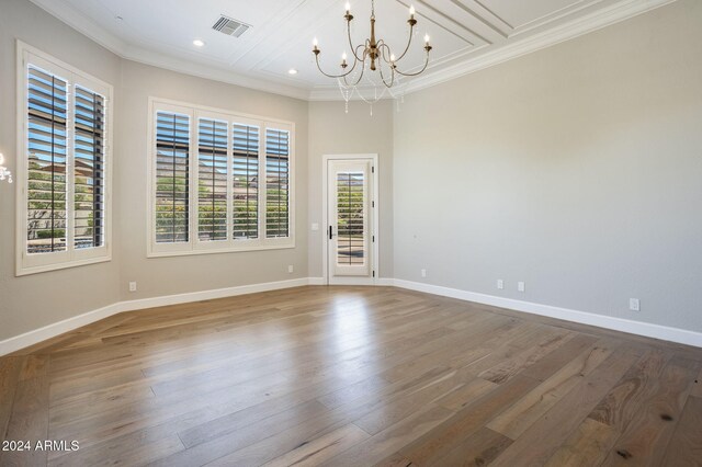 empty room with a wealth of natural light, hardwood / wood-style floors, and an inviting chandelier