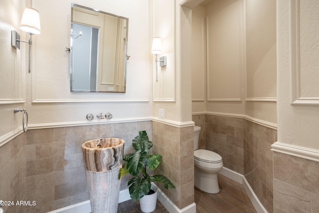 bathroom featuring wood-type flooring, tile walls, and toilet