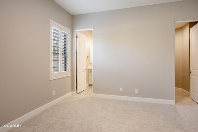 unfurnished bedroom with ensuite bath and light colored carpet