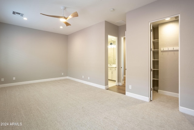 unfurnished bedroom featuring a walk in closet, ensuite bath, ceiling fan, light colored carpet, and a closet