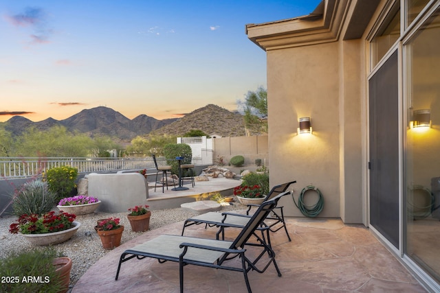 patio terrace at dusk with a mountain view and a fenced backyard