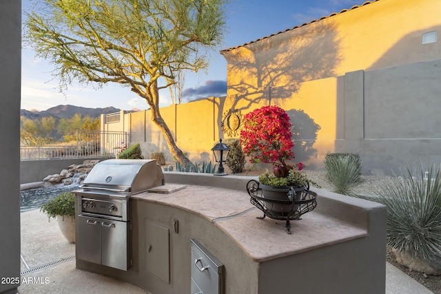 view of patio / terrace featuring a grill, exterior kitchen, fence, and a mountain view