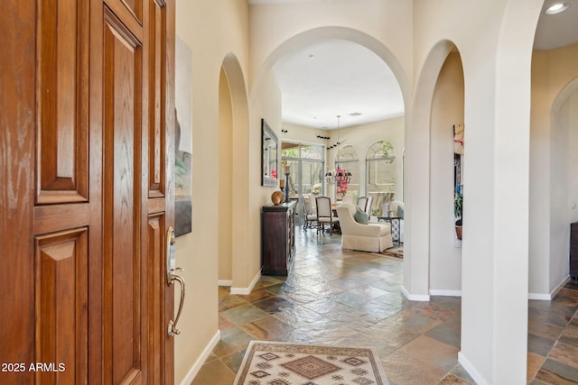 foyer featuring baseboards, arched walkways, and stone tile flooring