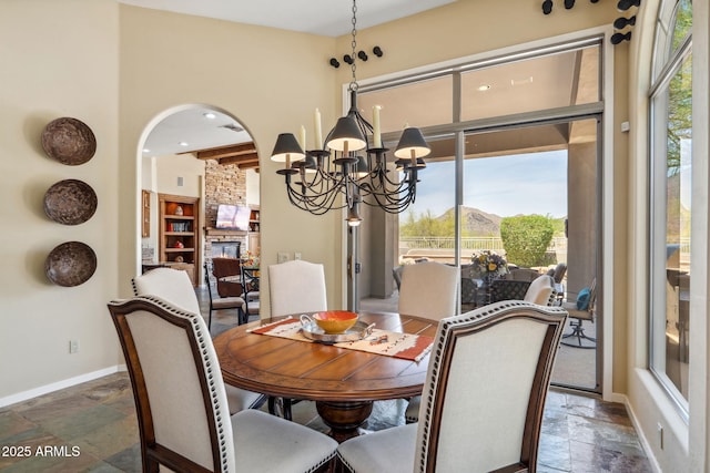 dining space featuring a notable chandelier, stone tile flooring, baseboards, arched walkways, and a fireplace