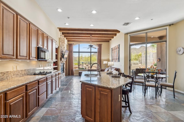 kitchen with a sink, visible vents, a healthy amount of sunlight, stone tile floors, and black microwave