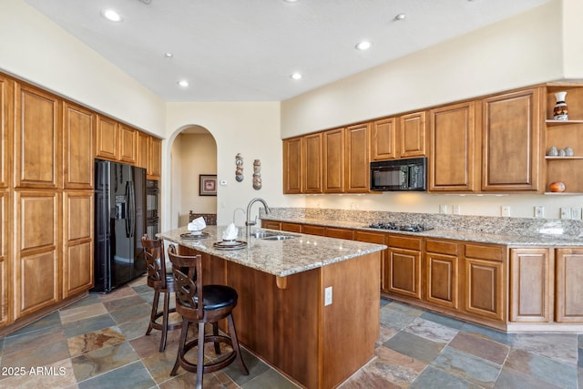 kitchen with stone finish floor, a sink, open shelves, arched walkways, and black appliances