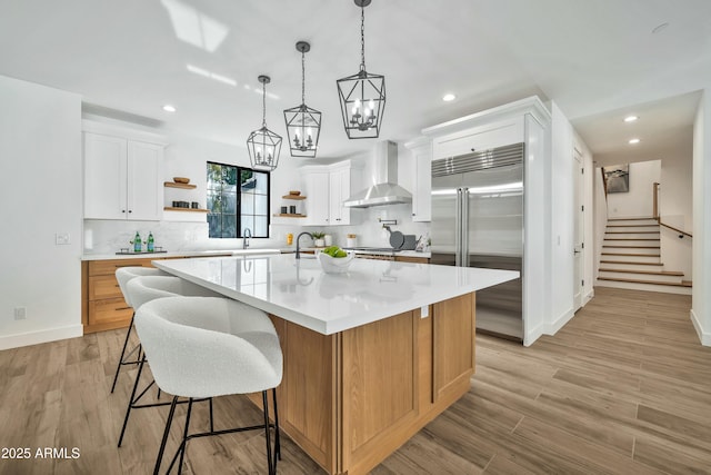 kitchen with white cabinets, a spacious island, wall chimney exhaust hood, and built in refrigerator