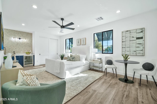 living room featuring ceiling fan, bar area, beverage cooler, and light wood-type flooring