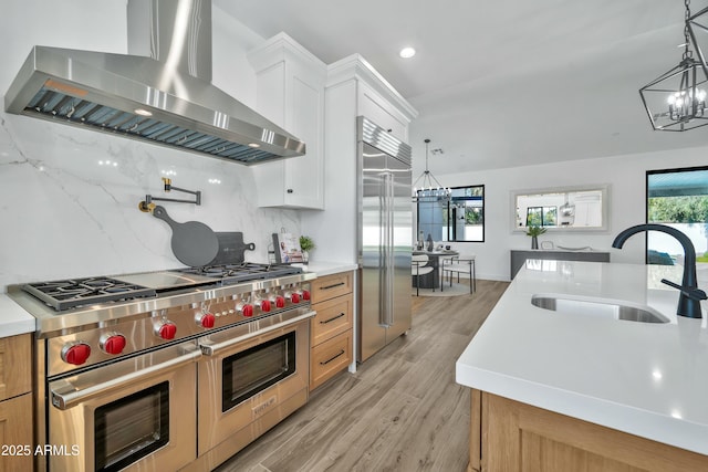 kitchen featuring ventilation hood, an island with sink, sink, white cabinets, and high end appliances