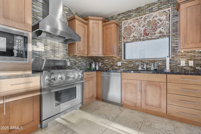 kitchen featuring appliances with stainless steel finishes, wall chimney exhaust hood, dark stone counters, sink, and backsplash