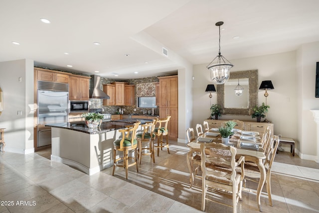 kitchen with a center island, wall chimney exhaust hood, decorative light fixtures, built in appliances, and tasteful backsplash