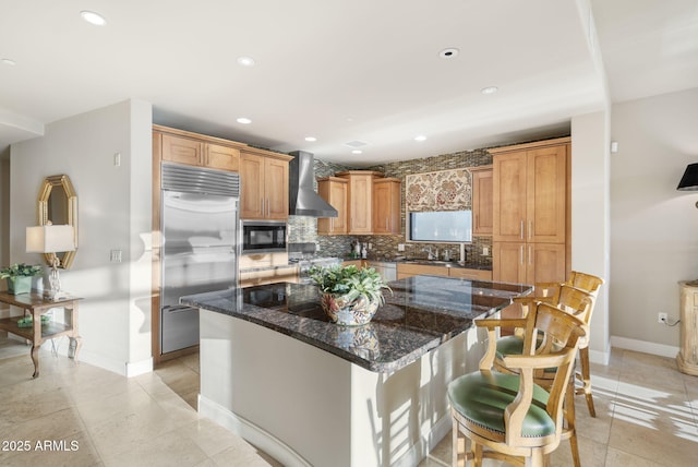 kitchen featuring wall chimney range hood, a center island, built in appliances, and tasteful backsplash