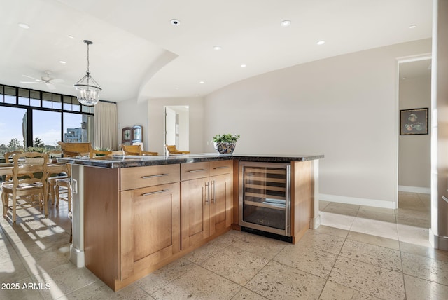 kitchen featuring wine cooler, ceiling fan, a kitchen island, pendant lighting, and dark stone counters