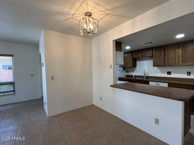 kitchen with a sink, dark countertops, a chandelier, dark brown cabinetry, and tile patterned flooring